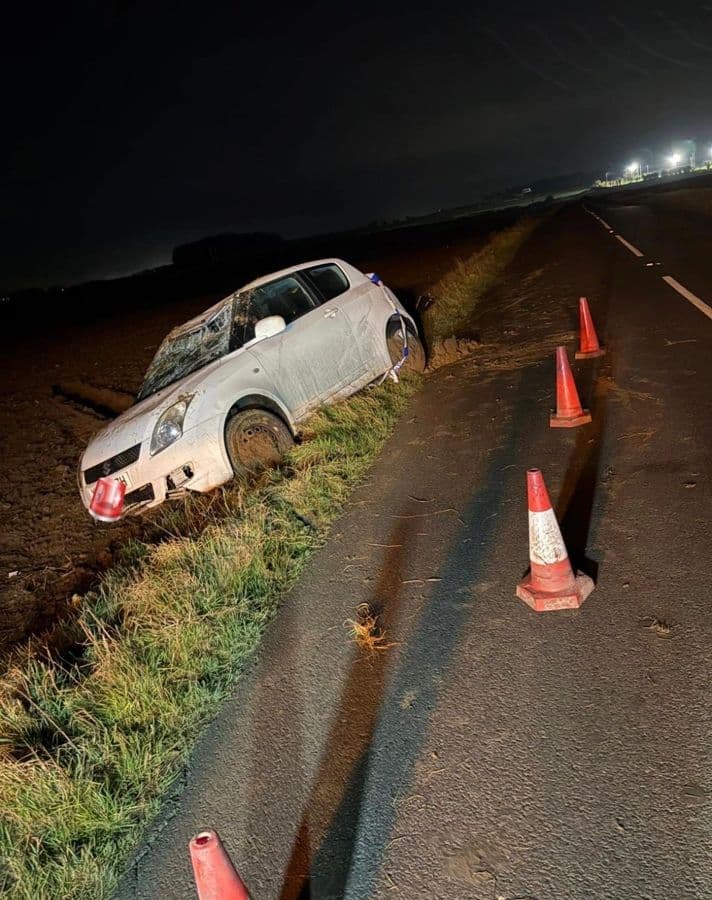 A car in a ditch at night with cones deployed on the carriageway